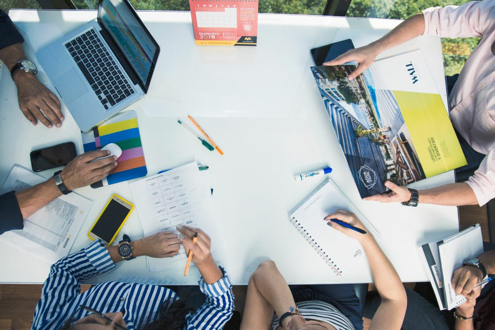 From above of crop unrecognizable coworkers gathering around table with laptop and papers while working together in office