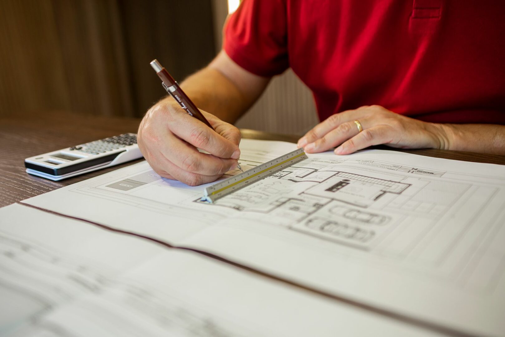 Architect working on floor plans with ruler and pencil in an office setting.