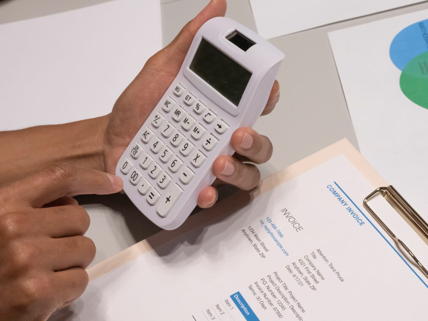 Close-up of hands using a calculator next to a company invoice, depicting a financial calculation concept.